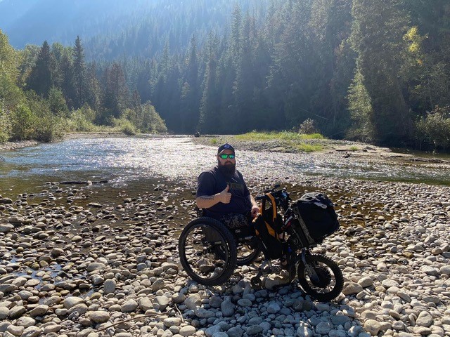 Man giving thumbs up in a mobility device in a riverbed
